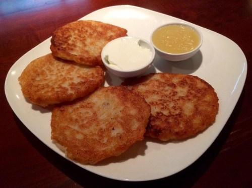 A plate of four golden-brown potato pancakes served with sour cream and applesauce.