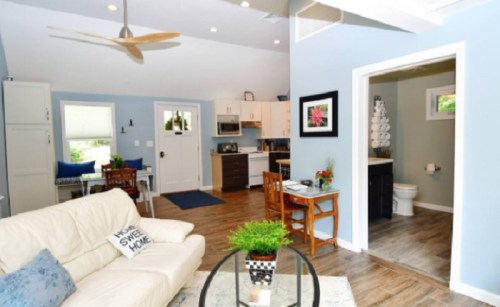 Cozy living space with a white sofa, dining area, and kitchen, featuring light blue walls and modern decor.