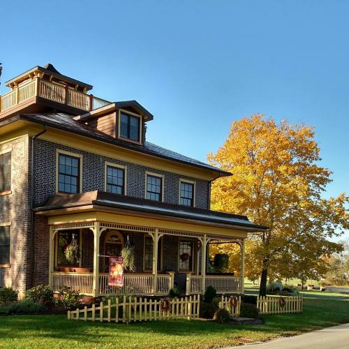 A charming two-story house with a porch, surrounded by autumn trees and a clear blue sky.