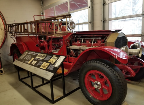 A vintage red fire truck displayed in a museum, showcasing its open engine compartment and historical information nearby.
