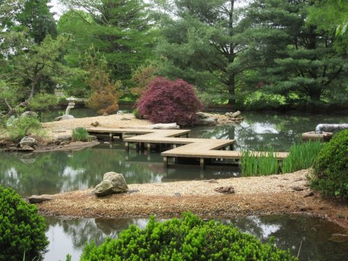 A serene garden scene featuring a wooden bridge over a pond, surrounded by lush greenery and colorful plants.