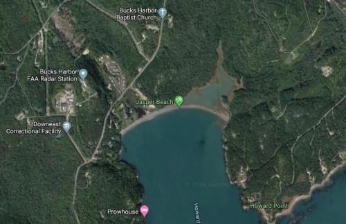 Aerial view of Jasper Beach, surrounded by forested land and nearby structures, including a church and a correctional facility.