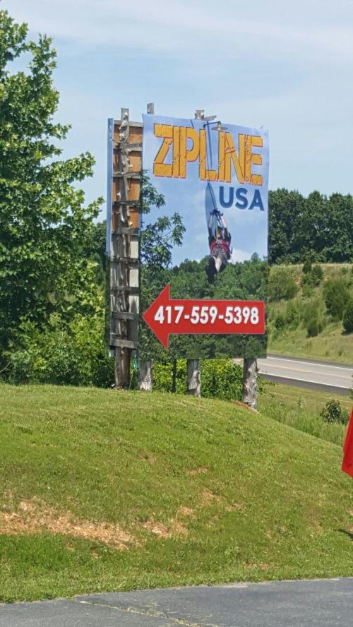Sign for Zipline USA featuring a zipline image and contact number, with an arrow pointing to the right.