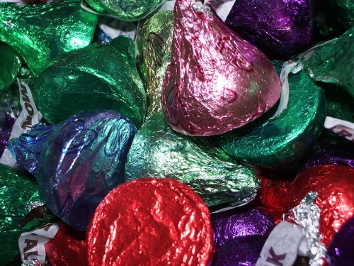 A colorful assortment of wrapped chocolate kisses in various shades of green, purple, red, and silver.