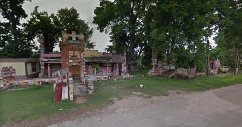 Abandoned, colorful building with unique architecture, surrounded by trees and overgrown grass.