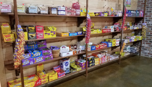 A colorful display of various candies and snacks on wooden shelves in a rustic store setting.
