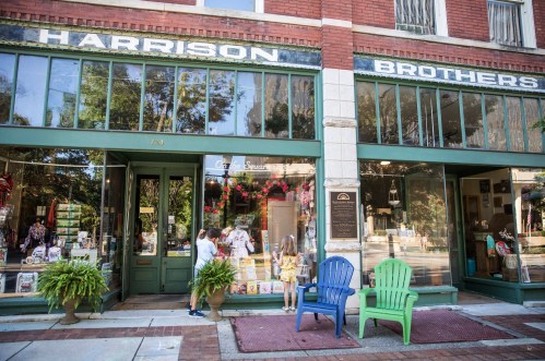 Two children look at a shop window while adults stand nearby, in front of a historic storefront with "Harrison Brothers" sign.