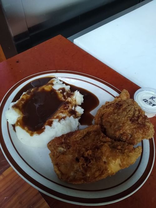A plate of fried chicken with mashed potatoes and gravy, served with a small container of sauce on the side.