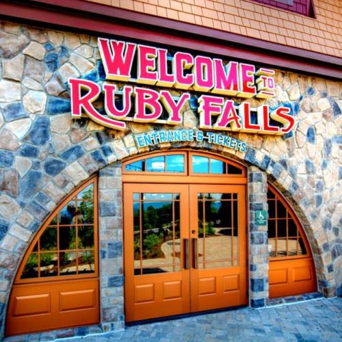 Sign for Ruby Falls with colorful lettering above a stone archway entrance and large glass doors.