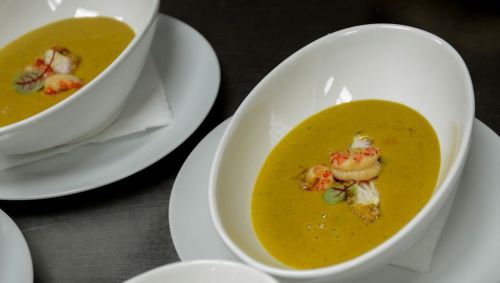 A bowl of yellow soup garnished with shrimp and fish, served on a white plate.