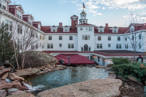 Historic hotel with a red-roofed tower, surrounded by greenery and a small pond, under a clear blue sky.