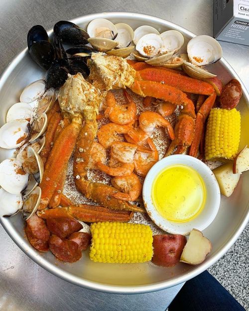 A seafood platter featuring shrimp, crab, mussels, clams, corn, potatoes, and a side of melted butter.