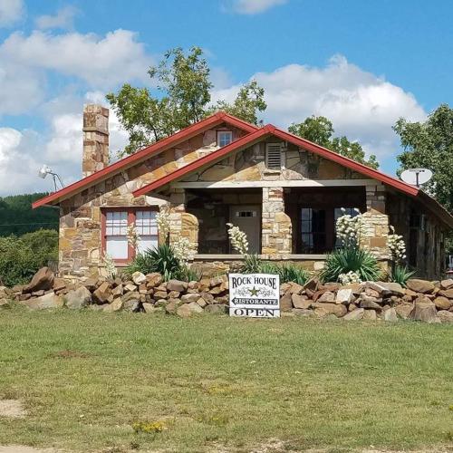 A stone building with a red roof and sign reading "Rock House Restaurant" surrounded by greenery and blue skies.