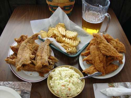 A table with fried fish, waffle fries, coleslaw, and a pitcher of beer.