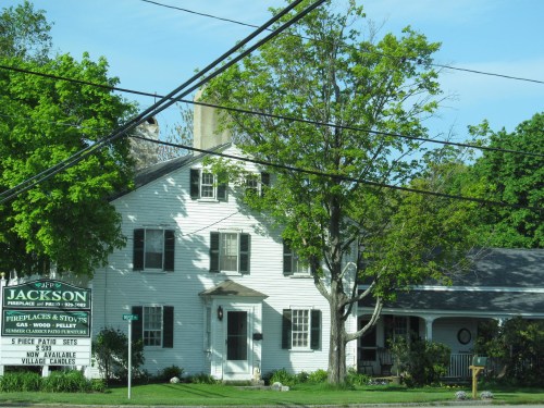 A white two-story house with green trees and a sign for Jackson's fireplaces and stoves in front.