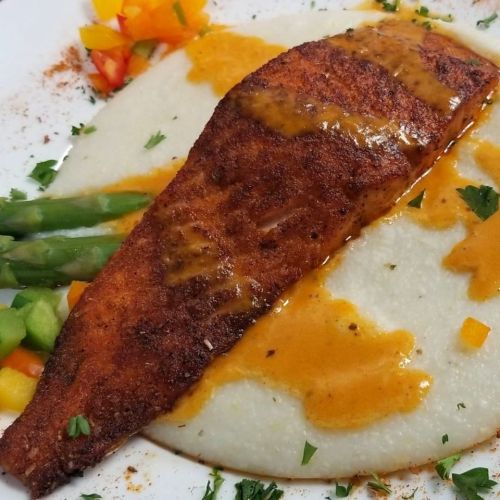A plate featuring a seasoned fish fillet on creamy grits, garnished with colorful diced vegetables and herbs.