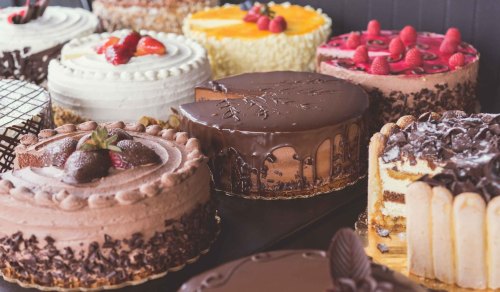 A variety of beautifully decorated cakes, including chocolate, fruit-topped, and layered options, displayed on a table.