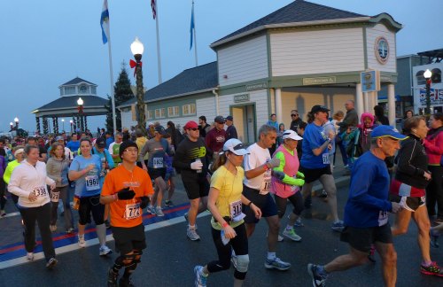 A crowd of runners in colorful attire participating in a race, with a building and flags in the background.