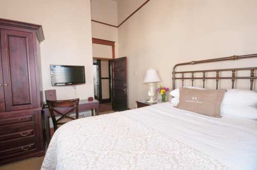 Cozy hotel room featuring a bed, wooden furniture, a TV, and a vase of flowers on a bedside table.