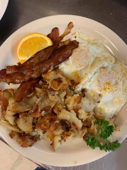 A plate of breakfast featuring two fried eggs, crispy bacon, golden hash browns, and a slice of orange.