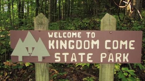 Sign welcoming visitors to Kingdom Come State Park, surrounded by lush green trees and foliage.