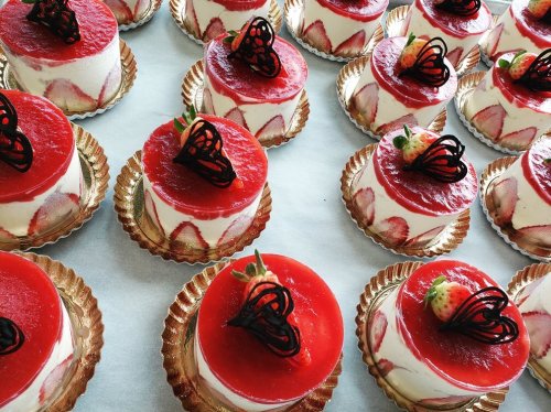 A display of individual strawberry cakes topped with red jelly and chocolate decorations on golden bases.