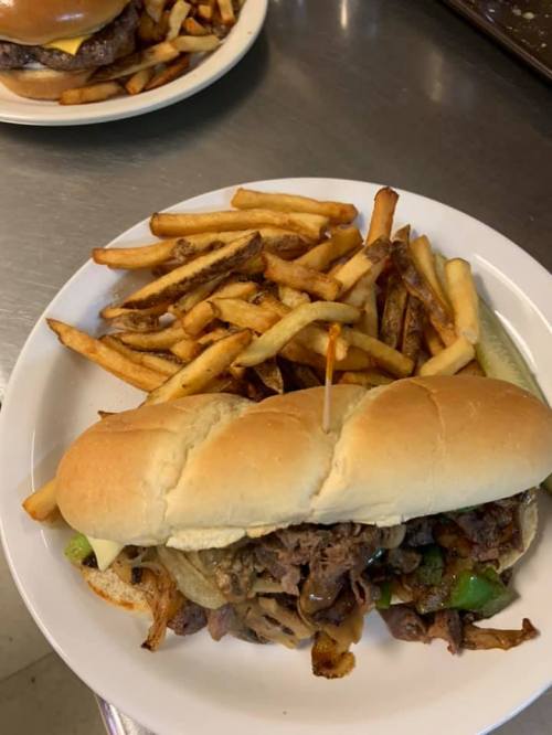 A plate with a sandwich filled with beef and peppers, accompanied by a side of crispy French fries.