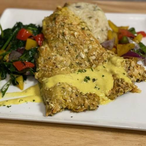 A plate featuring a baked fish fillet with a creamy sauce, served with rice and sautéed colorful vegetables.