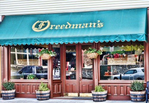 A storefront with a green awning reading "Freedman's," featuring potted plants and decorative window displays.