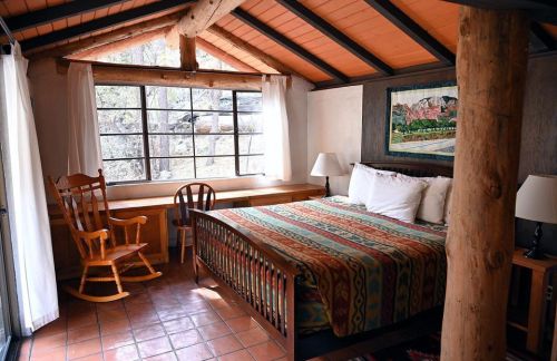 Cozy bedroom with a wooden bed, rocking chair, and large windows letting in natural light. Colorful patterned bedding.