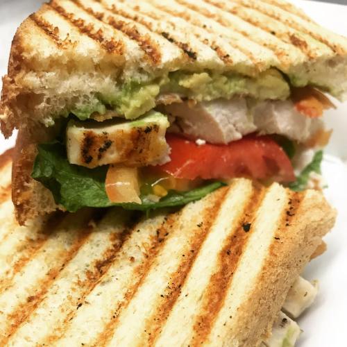 Grilled sandwich with chicken, avocado, lettuce, tomato, and toasted bread, cut in half to show filling.
