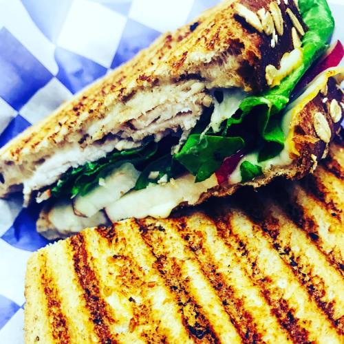 A toasted sandwich with layers of turkey, cheese, lettuce, and tomato, served on a blue and white checkered paper.