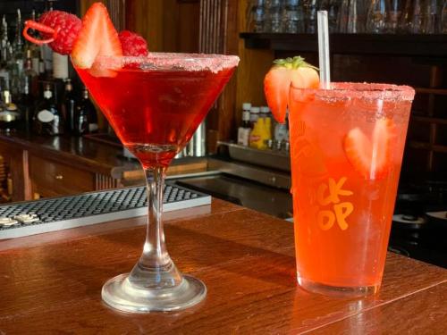 Two colorful cocktails on a bar: a red martini with raspberries and a strawberry drink in a clear glass.