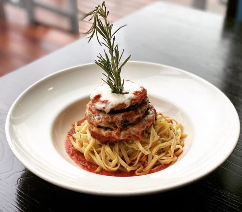 A plate of pasta topped with layered eggplant, marinara sauce, cheese, and a sprig of rosemary.