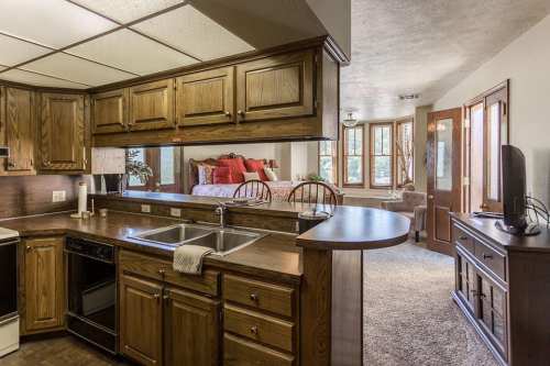 A cozy kitchen with wooden cabinets, a double sink, and an open layout leading to a living area with natural light.