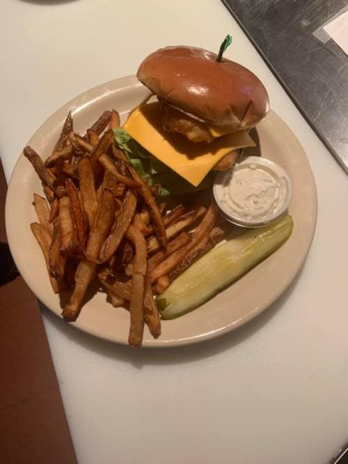 A plate with a cheeseburger, crispy fries, a pickle, and a side of dipping sauce.