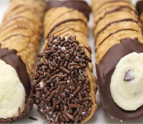 Close-up of cannoli filled with cream, some dipped in chocolate and topped with chocolate sprinkles.
