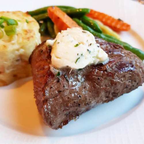 A plate featuring a grilled steak topped with herb butter, alongside green beans, carrots, and a potato dish.