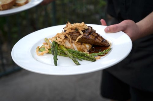 A plate of grilled meat topped with crispy onions, served with asparagus and a creamy sauce.