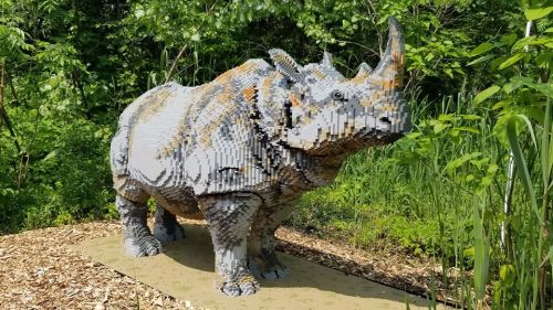 A large, pixelated sculpture of a rhinoceros made from colorful blocks, set in a lush green outdoor environment.