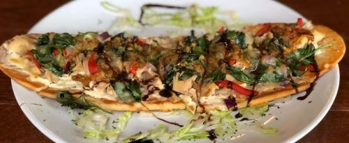 A flatbread topped with chicken, spinach, red peppers, and drizzled with balsamic glaze, served on a bed of lettuce.