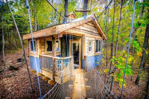 A charming treehouse nestled in a forest, connected by a wooden walkway and surrounded by vibrant autumn foliage.