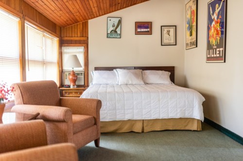 Cozy bedroom featuring a bed, two armchairs, and vintage wall art in a warm, inviting atmosphere.