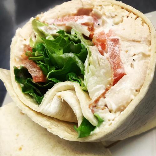 A close-up of a fresh wrap filled with lettuce, tomatoes, and chicken, served on a plate.