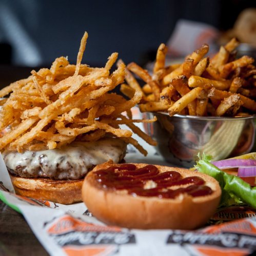 A juicy burger topped with crispy onion strings, served with a side of golden fries and a bun with ketchup.