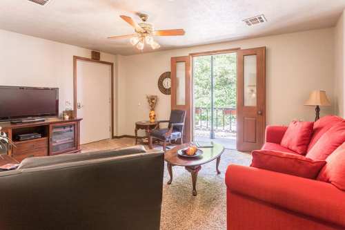 Cozy living room with a red sofa, TV, coffee table, and a door leading to a balcony. Natural light from the window.