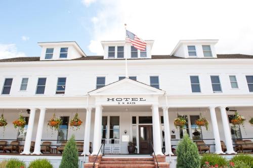 A charming white hotel with a flag, featuring a porch and flower baskets, set against a bright sky.