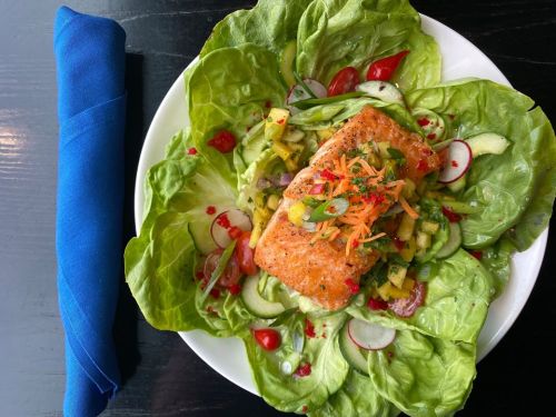A vibrant salad topped with grilled salmon, avocado, and colorful vegetables on a bed of leafy greens.
