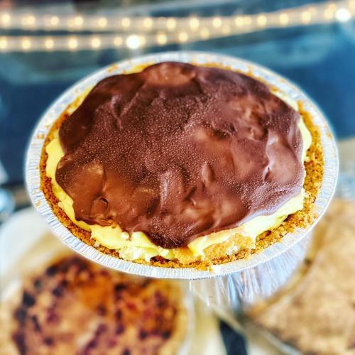 A close-up of a chocolate-topped pie with a golden crust, set against a blurred background of lights.