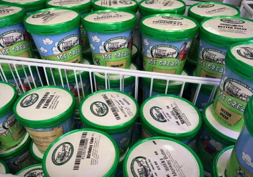 A display of colorful ice cream tubs in a freezer, featuring various flavors like vanilla, chocolate, and butter pecan.